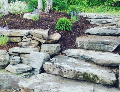 Large natural stone retaining wall with built-in stone steps and a planted bed on top