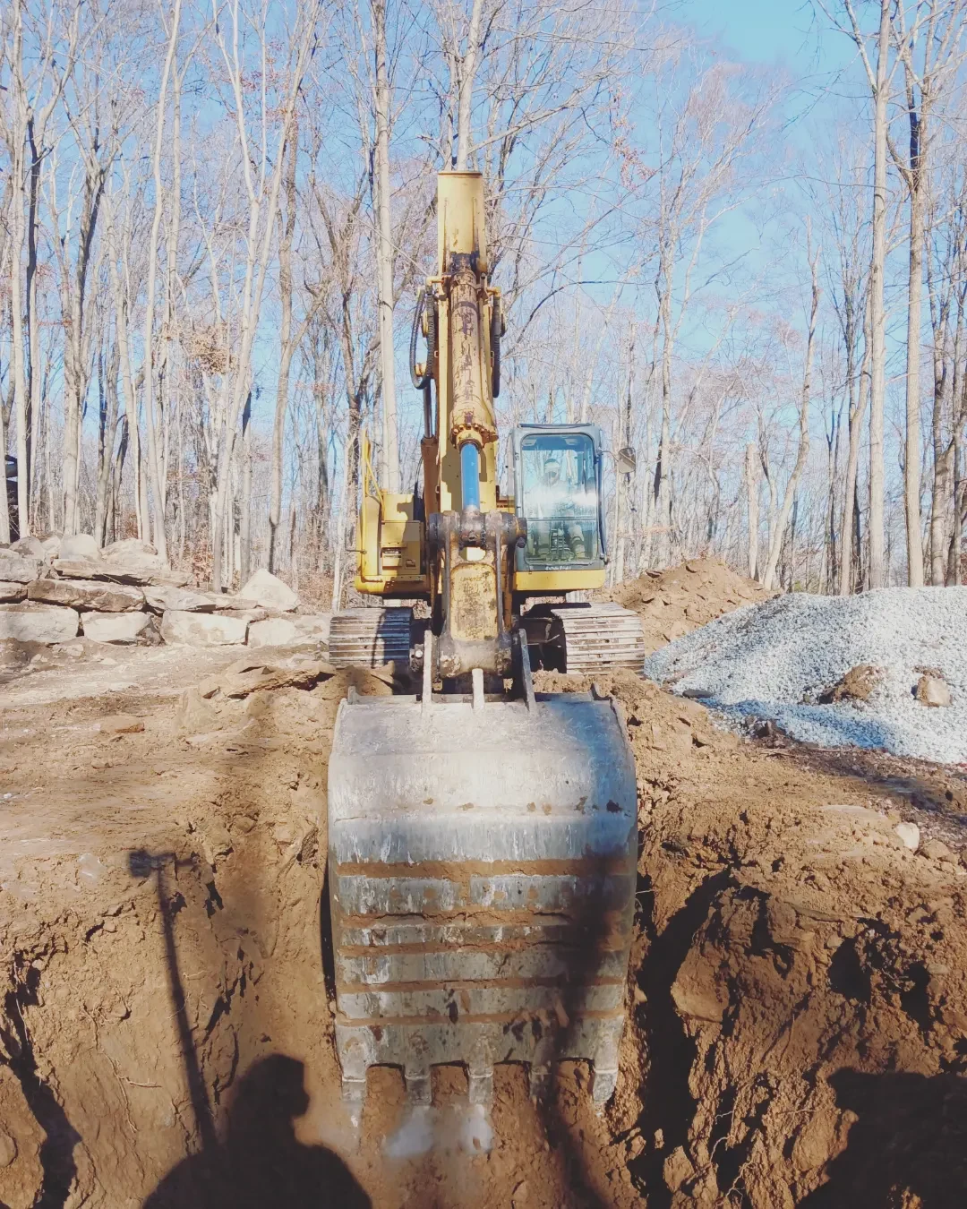 Excavator digging a roadside drainage ditch alongside a gravel driveway