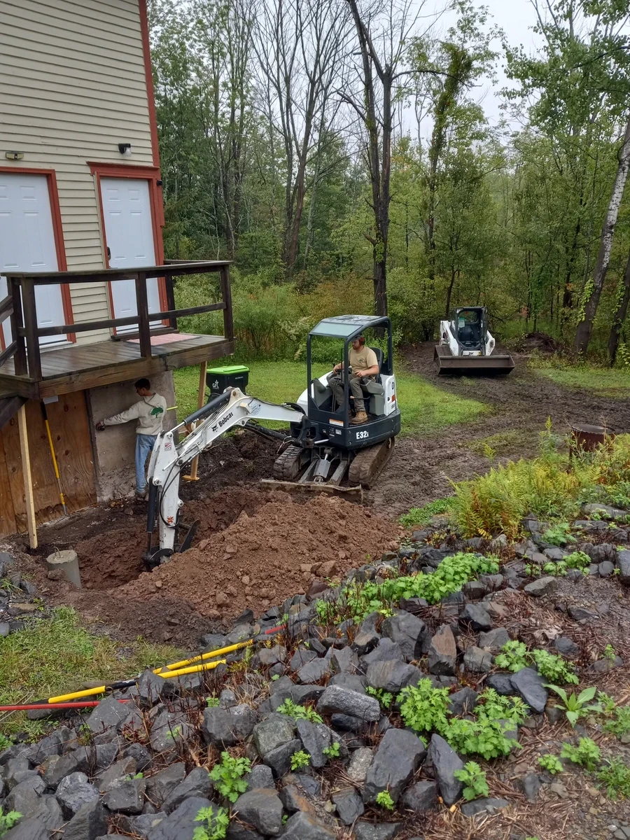 Mini excavator digging a drainage trench along the foundation of a house