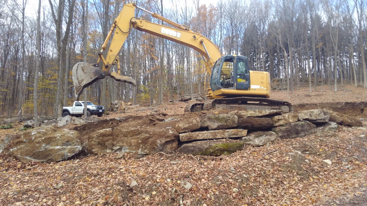 Excavator placing large rocks to build a stone retaining wall on a wooded NEPA property