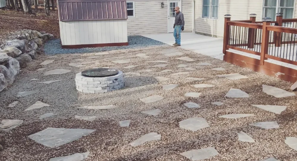 Flagstone patio with a stacked stone fire pit installed behind a home's deck