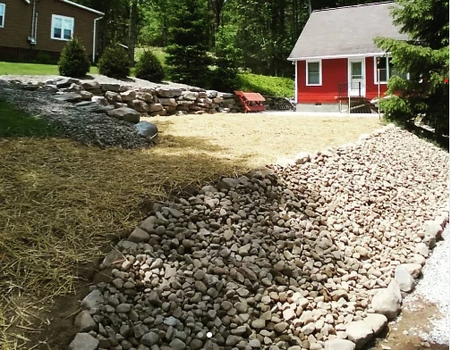 River rock drainage swale running through a freshly hydroseeded yard