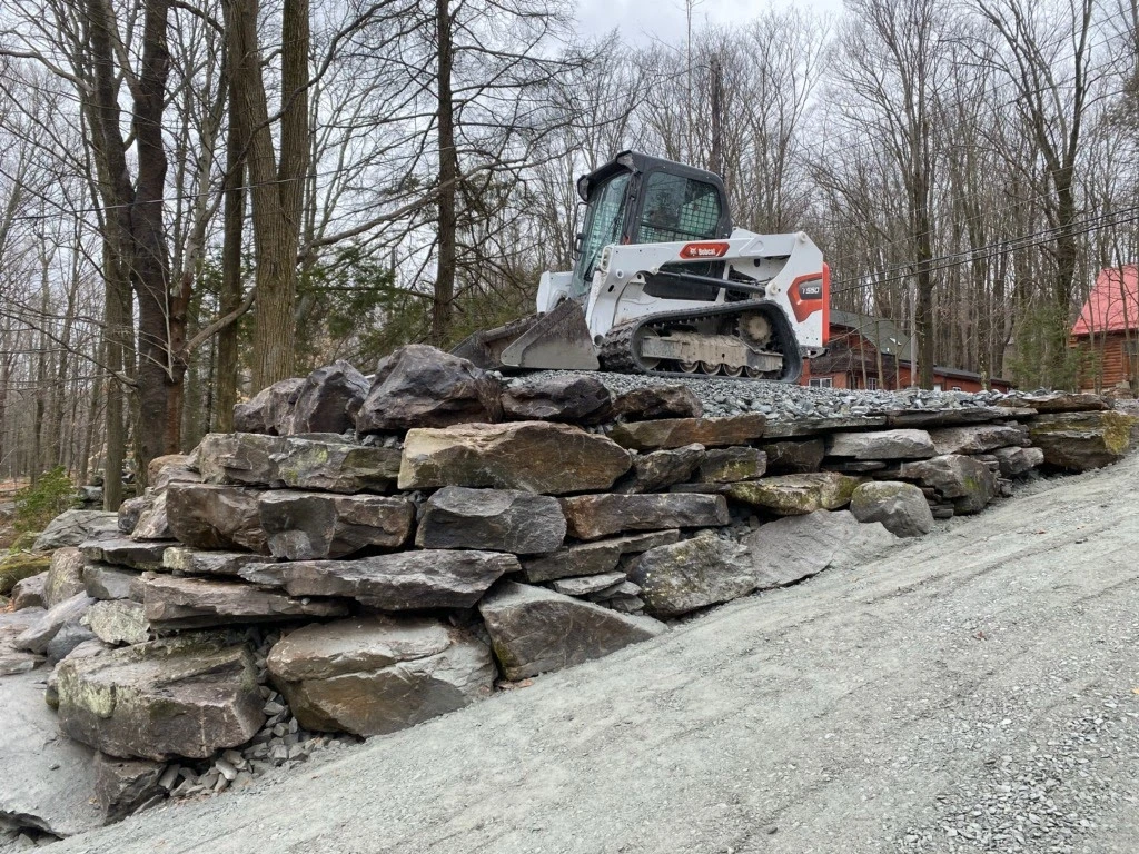 Large boulder retaining wall built into a hillside, creating a flat lawn area above