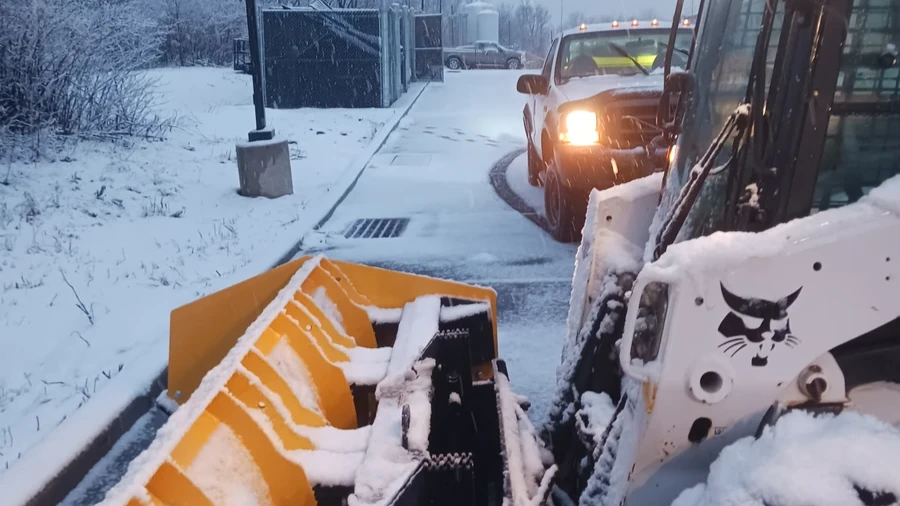 Skid steer with plow attachment clearing a commercial parking lot