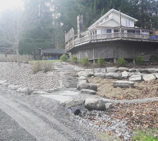 Natural stone steps and stacked stone wall built into a hillside leading up to a home's deck